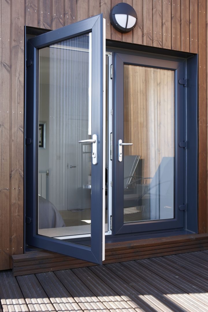 Anthracite grey french doors open on a timber-clad house